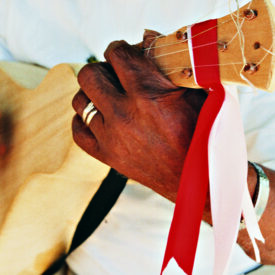 mão segurando cordas de violão ou instrumento similar, na ponta existem dois fetilhos