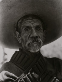 Fotografia em preto e branco, PB. Homem maduro usando chapéu sombreiro. Fotografia de perfil, pele com traços de idade marcados, bigode grosso formando cavanhaque. Homem zapatista trajando porta munição